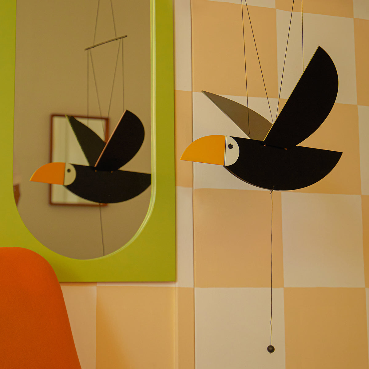 Areaware Toucan Mobile flying next to green mirror in front of checked wall
