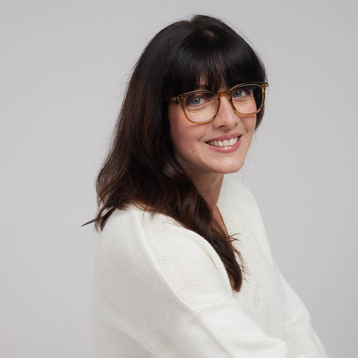 Woman wearing Izipizi shape e golden green reading glasses with cream jumper and long brown hair