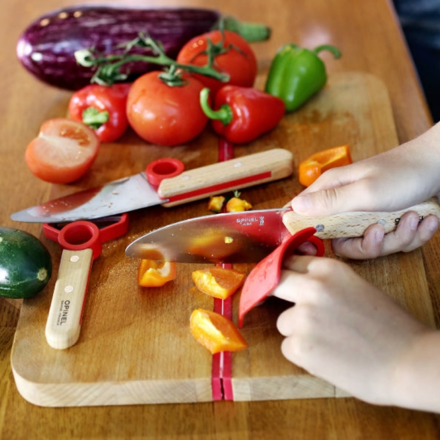 Child using Opinel Le Petit Chef 3pc Set SS Red on chopping board cutting up various vegtables