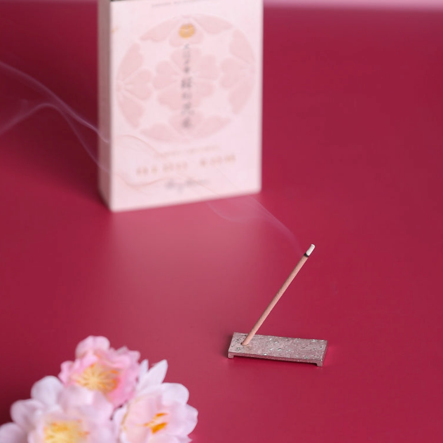 Oedo-Koh Incense Cherry Blossoms on display burning with incence out of packaging stood in included incense stand with pink background and cherry blossoms infront