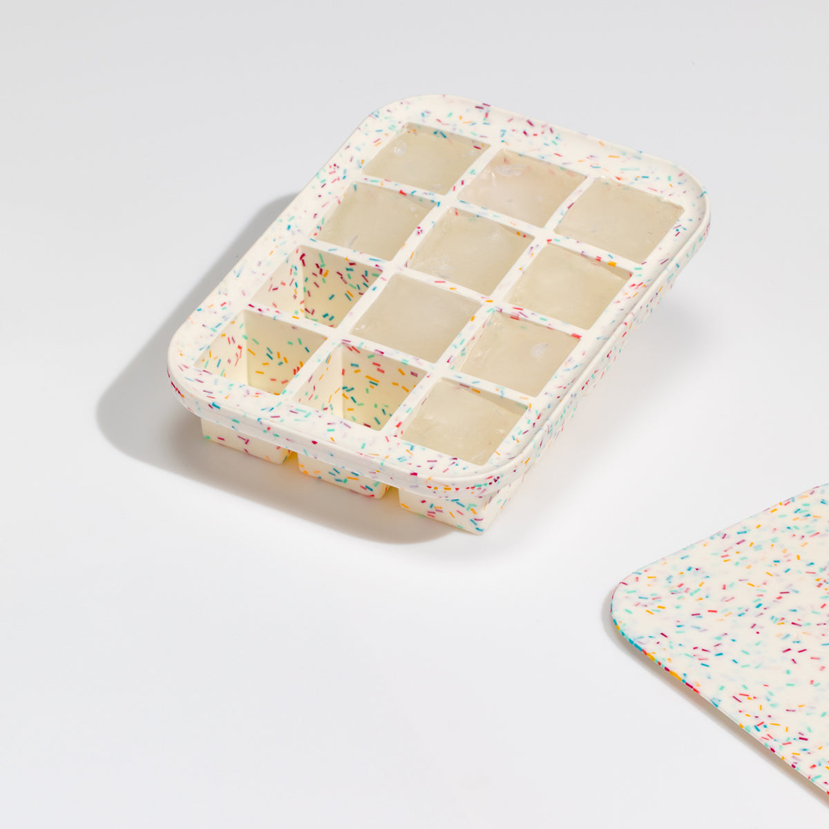 WP white speckled everyday ice cube tray on a white table with lid laying next to it