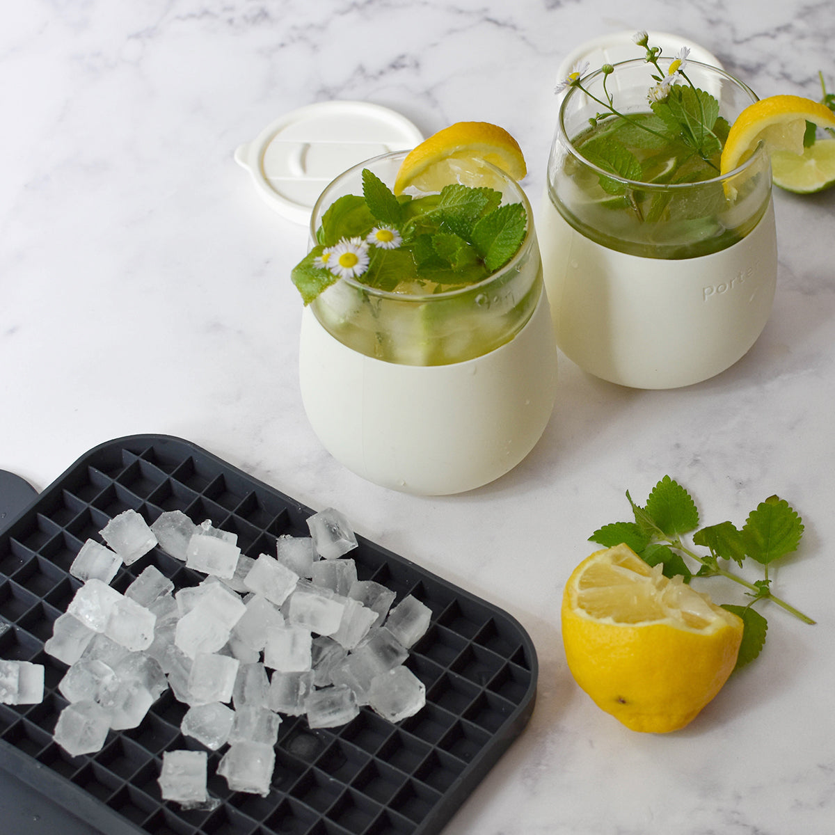 WP pebble ice cube tray full of pebble ice next to two glass and cream silicon cuts with mint ice and lemon