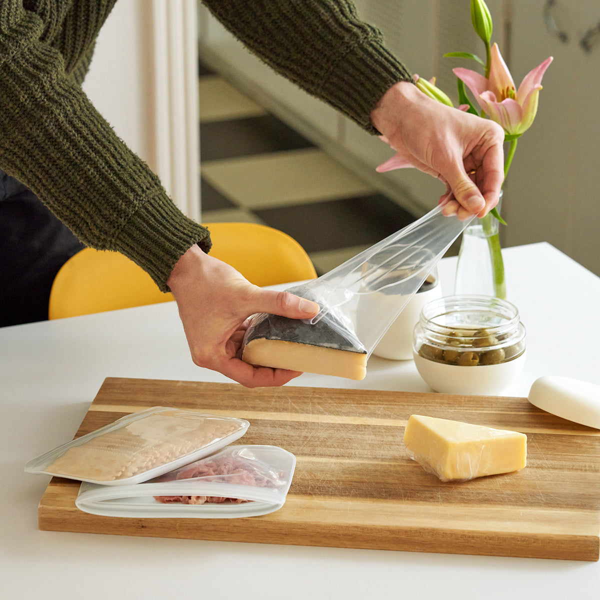 Woman wearing olive jumper covering cheese with WP set of 3 reusable stretch wrap ove wooden cheese board