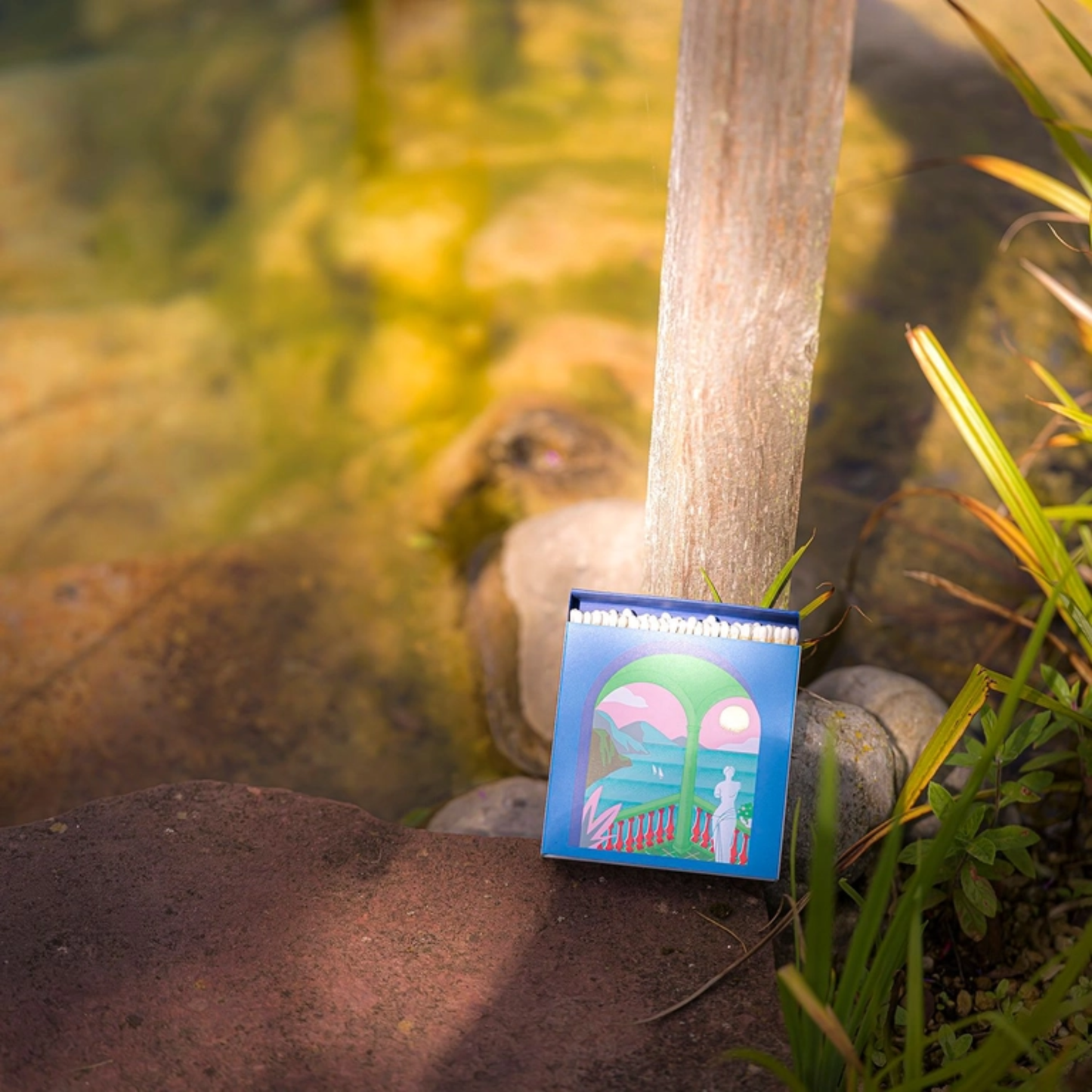 On the grounf leaning in a small plant Archivist A Romantic View Matches - Square Green Balcony Design Matchbox with Gold Foil Sunset - 125 Natural White-Tipped Matches in Blue Tray - FSC Wood, UK Made, Eco-Friendly Gift Decor