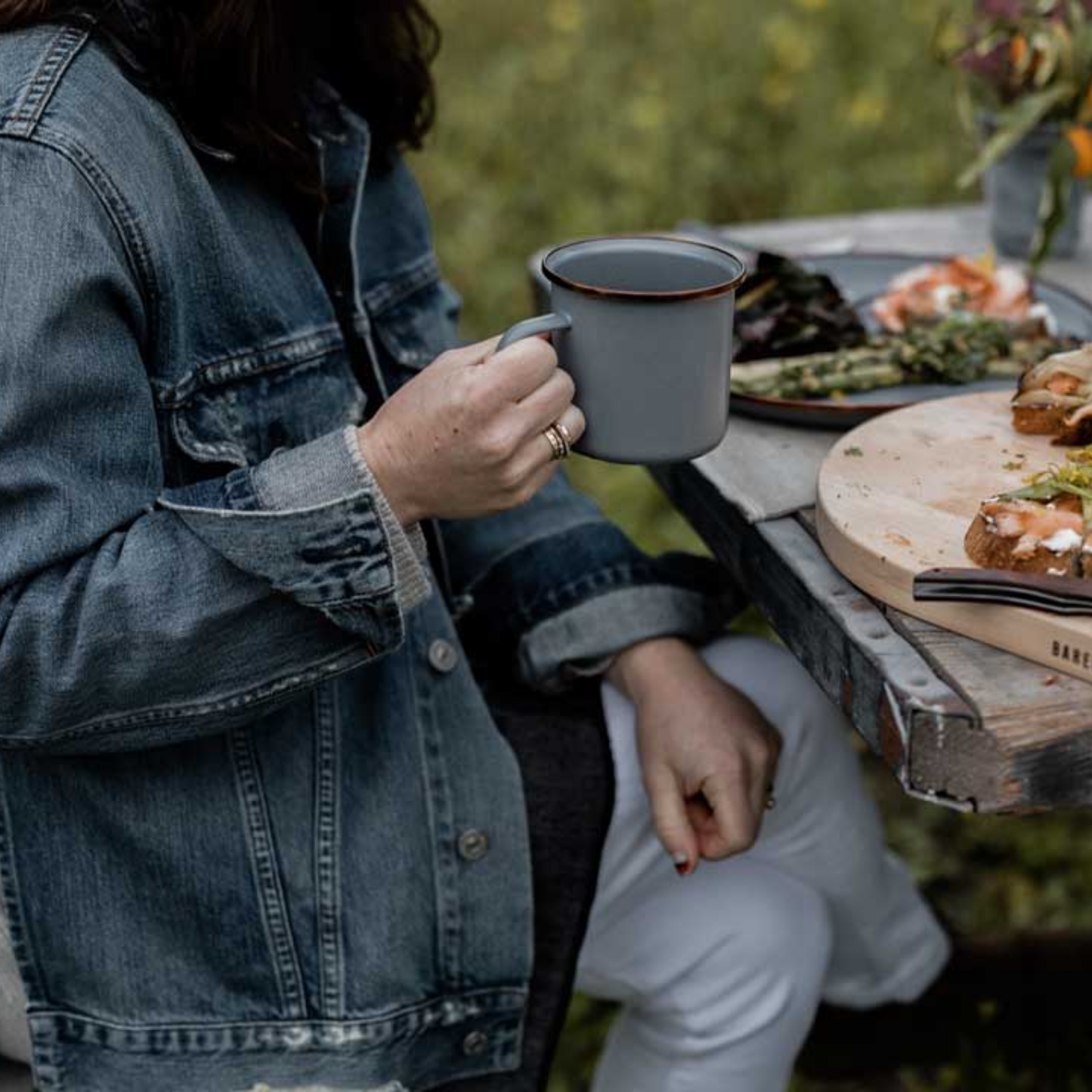 Woman holding slate grey Barebones enamel cup at outdoor table