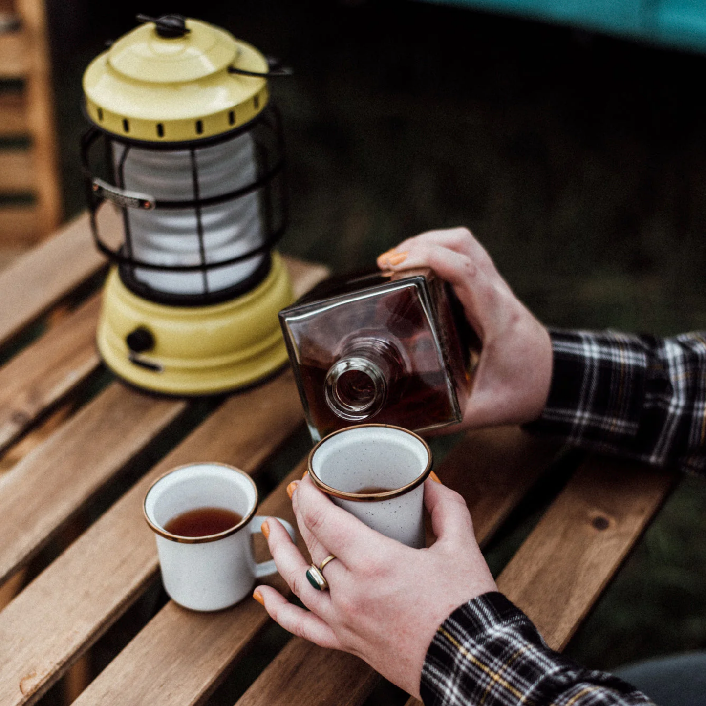 Barebones enamel eggshell espresso cup on ouside table with yellow lamp with woman pouring liquid in to cup