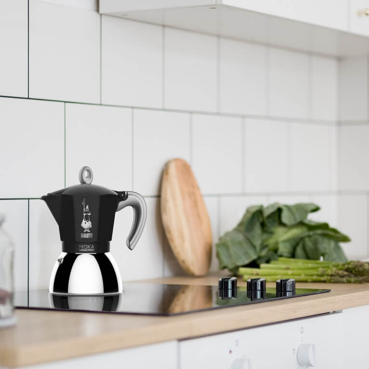 Shown on the table Bialetti Moka Induction stovetop espresso maker, 6-cup capacity, featuring an aluminum upper chamber and bi-layer steel base for use on induction hobs, combining classic Italian design with modern brewing performance.