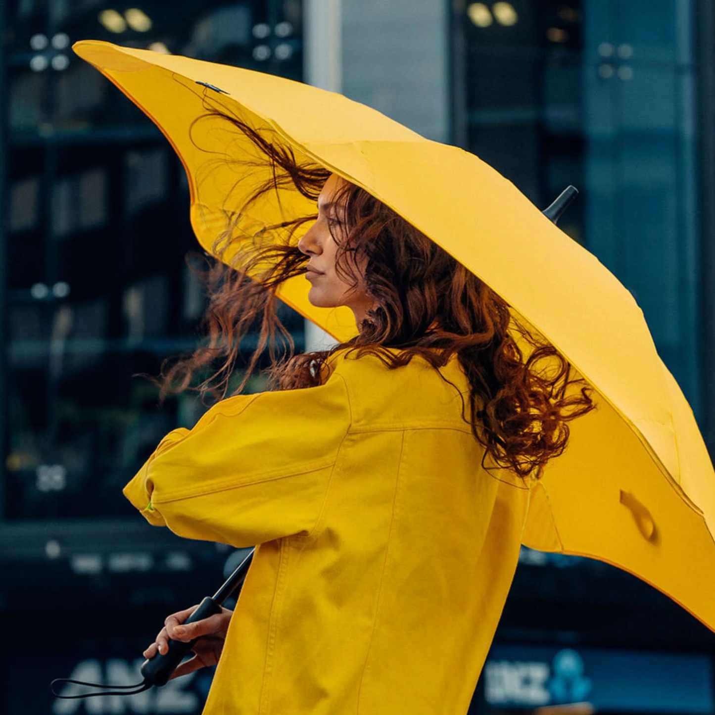 Another view of a woman using the Blunt Umbrella Classic Citrus Yellow in original full length that consist of the detachable UV fabric canopy, sturdy frame, shaft and handle. Ideal protection from heavy downpour or any weather.