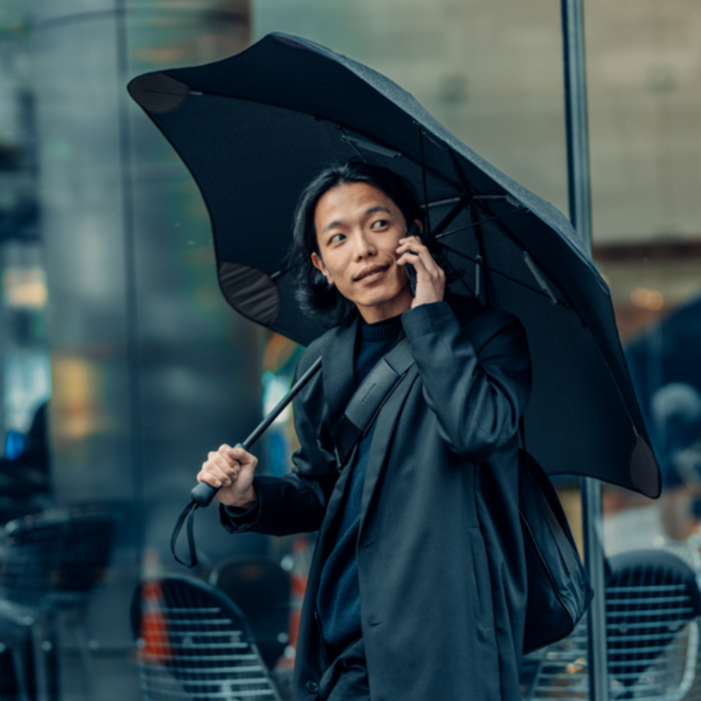 Person crossing road on phone holding open Blunt classic ink black umbrella over shoulder