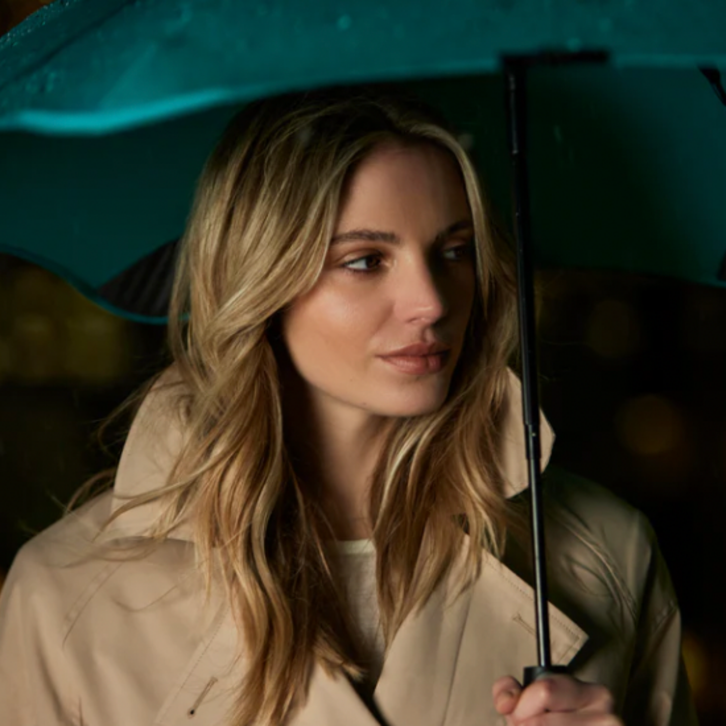 Woman holding Blunt mint classic umbrella open over her shoulder in dark lighting
