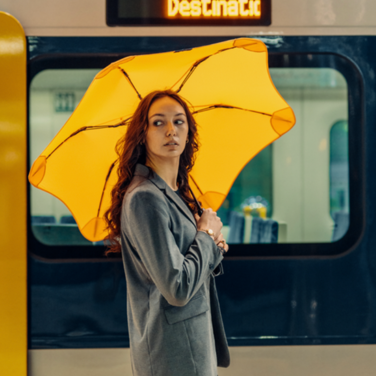 Woman posed infront of train with Blunt citrus yellow metro umbrella