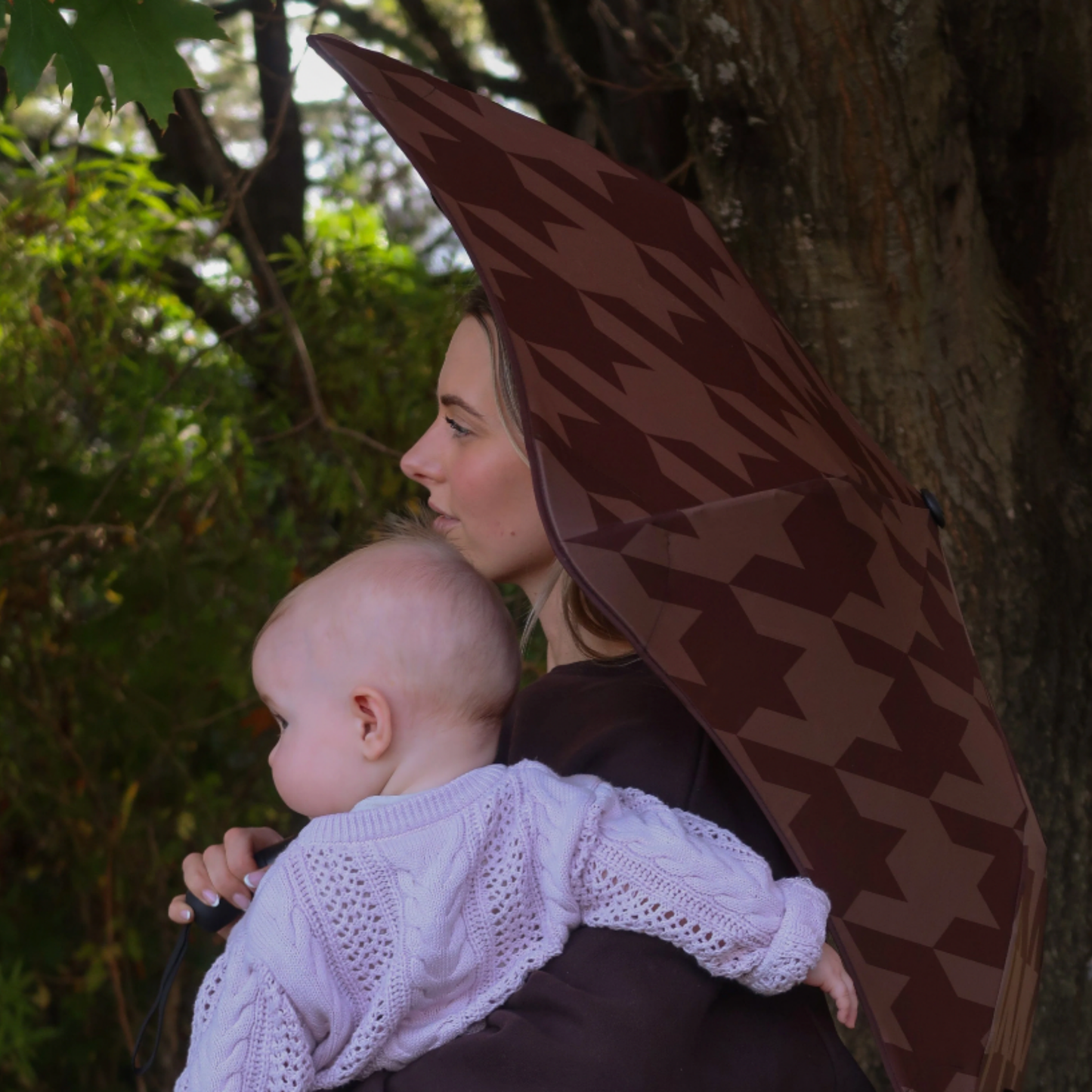 Woman holding baby and Blunt metro houndstooth umbrella over shoulder