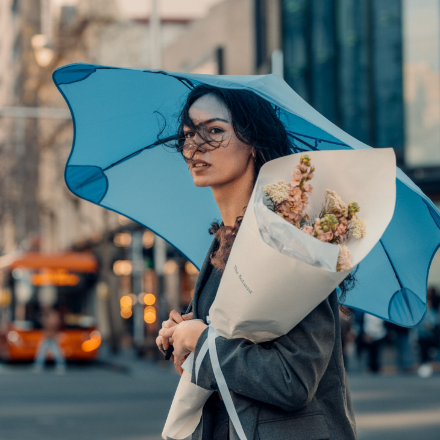 Woman holding flower bouquet and blunt metro sky blue crossing street in city