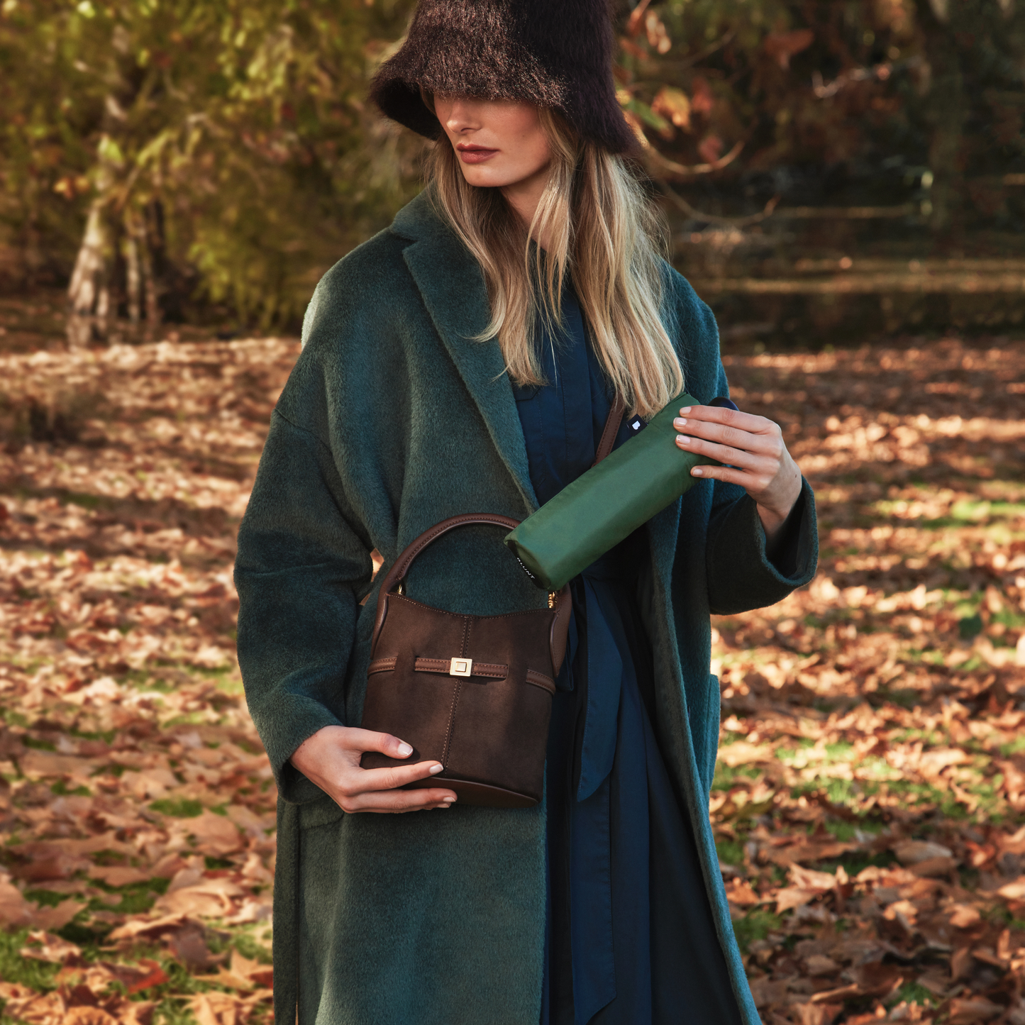 A woman putting the folded Blunt Umbrella Forest Green in to her bag, which features a compact design with high tensioned canopy, wind tested construction and recycled rPET fabric for rain or shine.