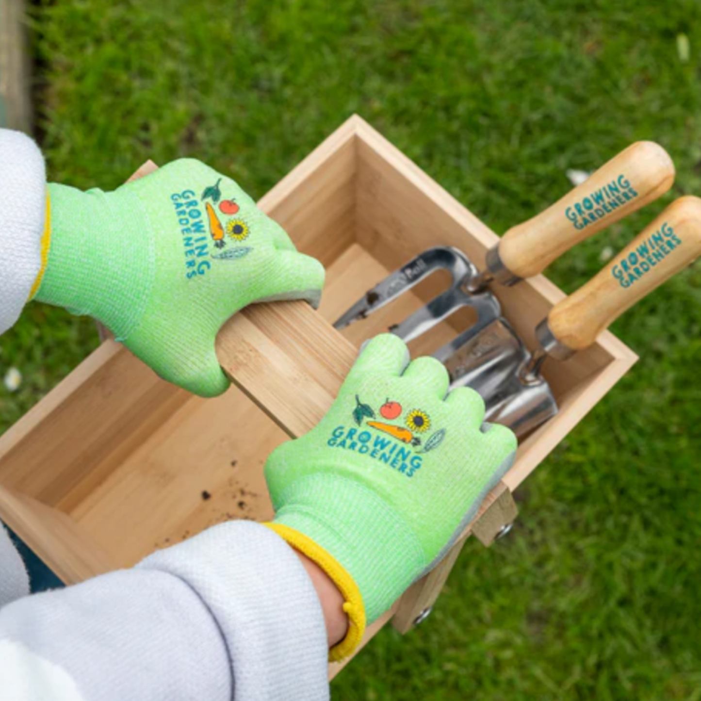 Little kid wearing Burgon & Ball kids gardening gloves holding wooden harvesting basket outside