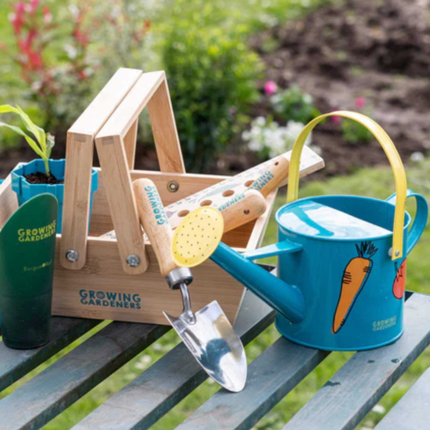 Burgon & Ball national trust kids watering can outside on wooden table with plants and terracota pots