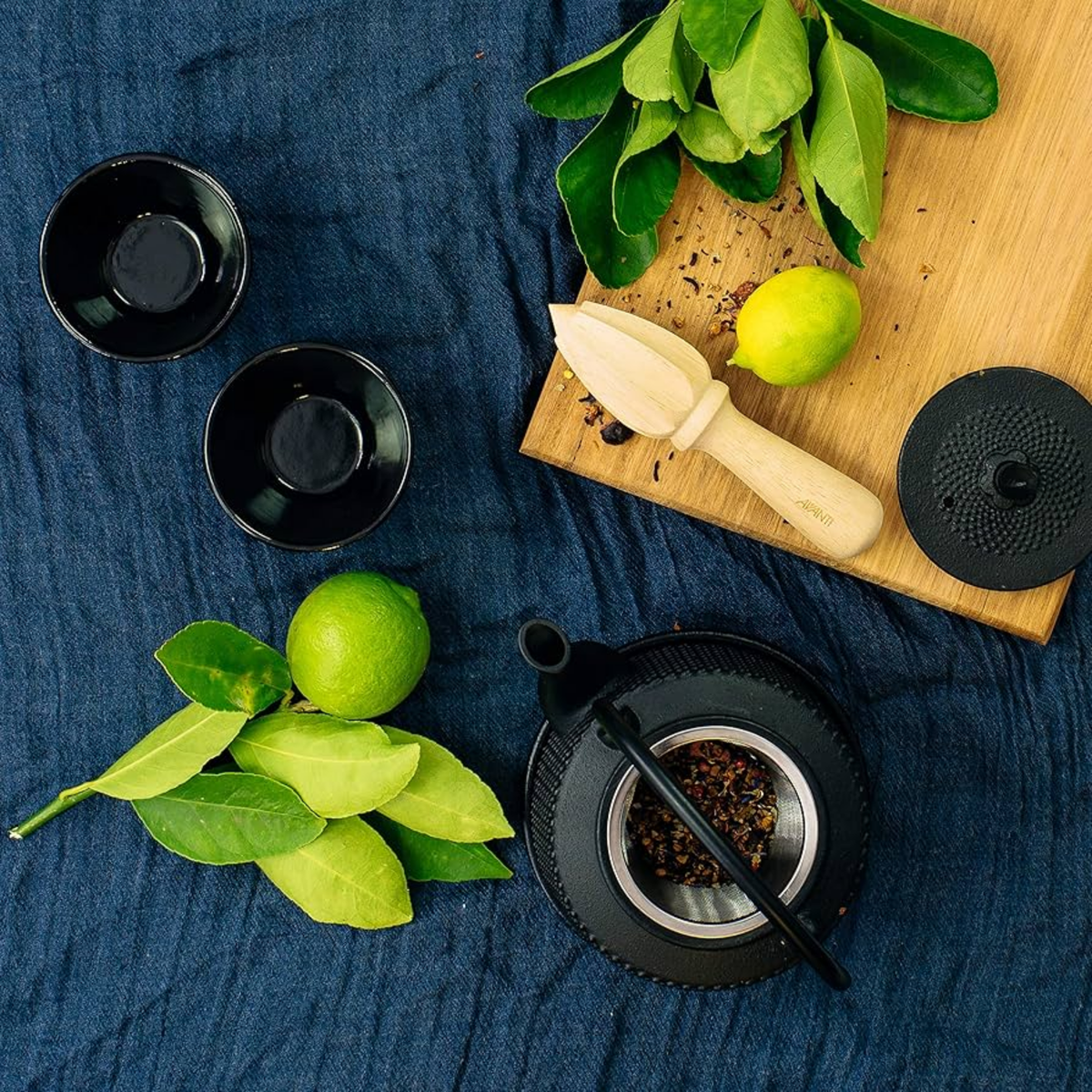 Wooden hand held citrus reamer side view on chopping board with lemons and limes and teapot