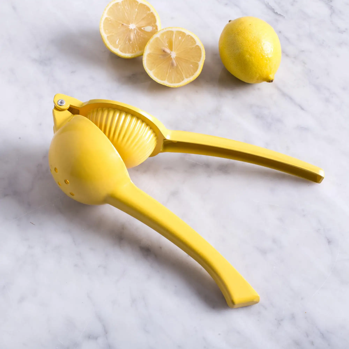 Yellow metal lemon squeezer on the side half open on marble table wioth lemons