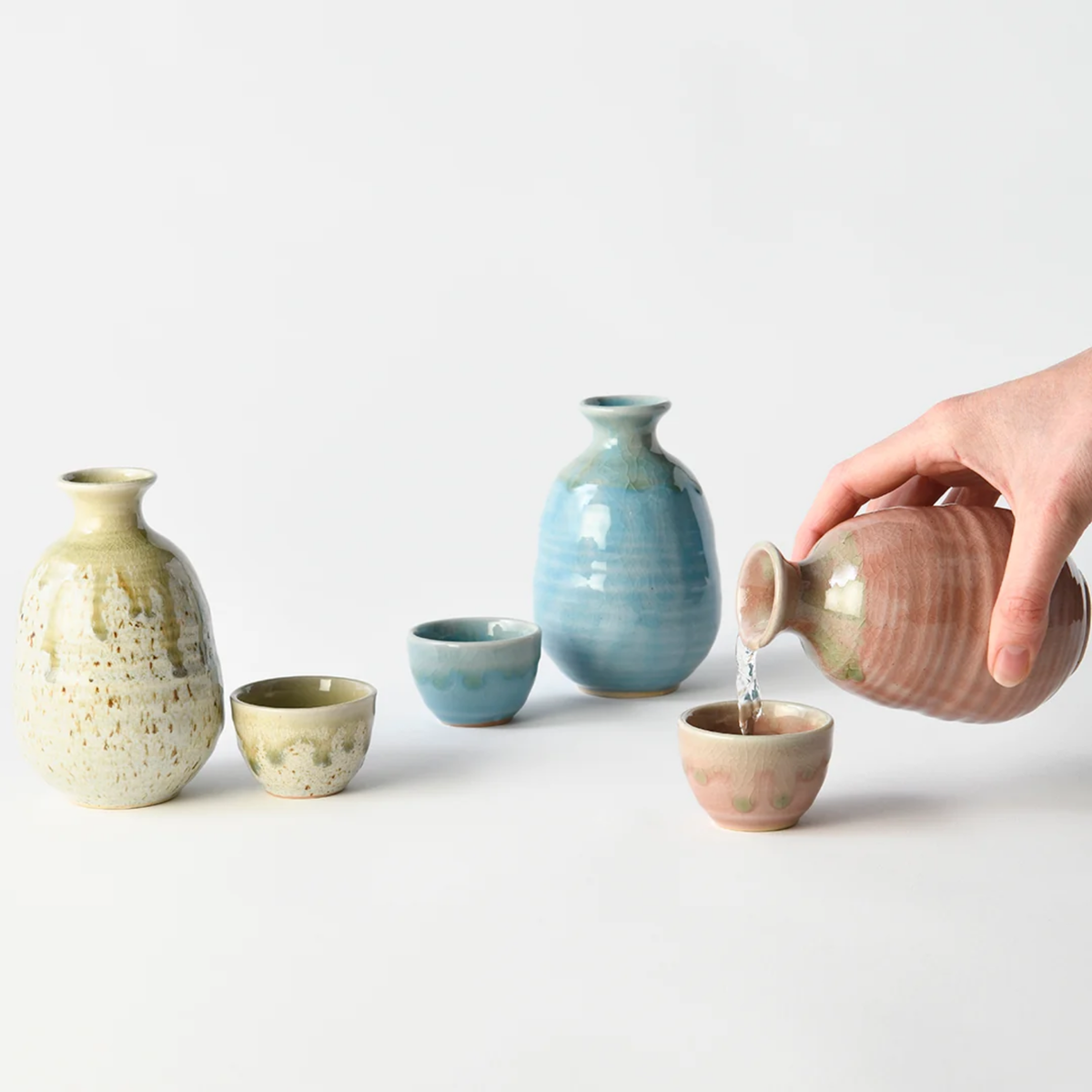 Three variants of jug with the Fathom Japanese Sake Jug in light green, ceramic with drip glaze, rounded body and narrow neck for smooth pouring.