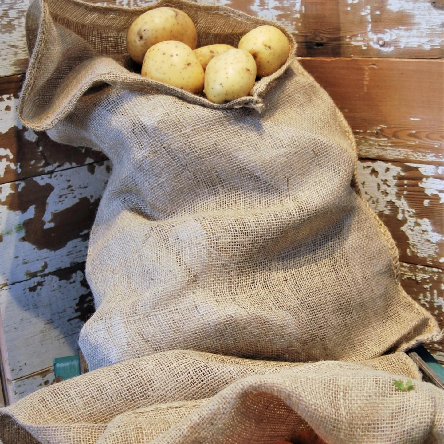 Jute storage bag containing potatoes leanomg against wooden crate