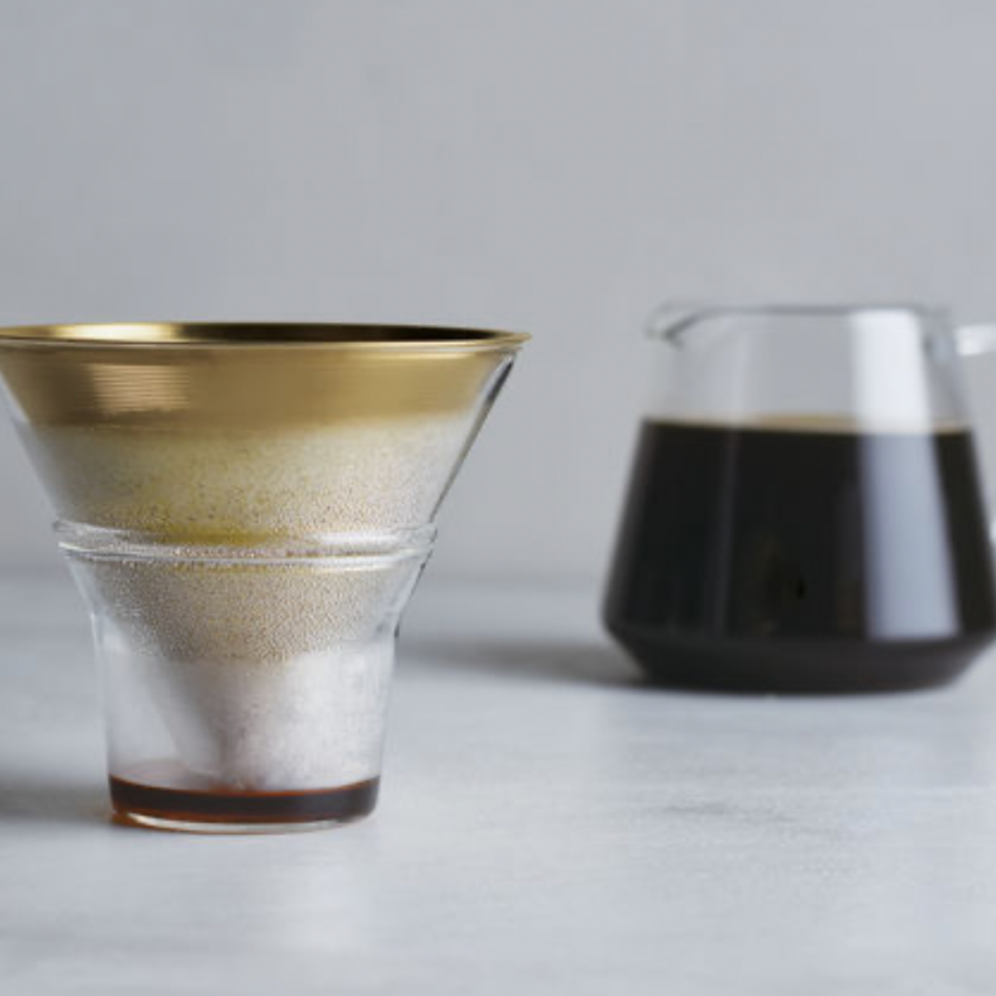 Coffe on display with the Glass drip dish at foreground with filter in it and cofee jug in background