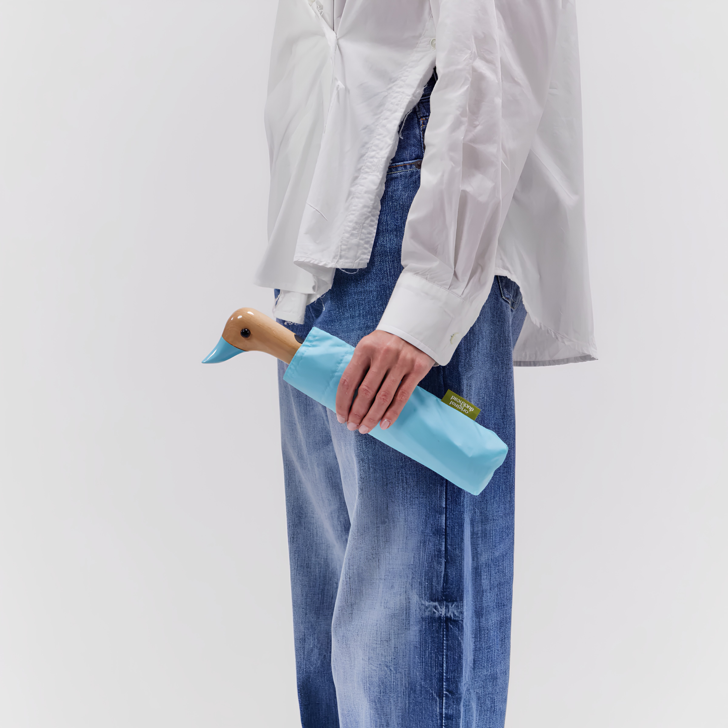 Kept inside its little pouch and held by a woman, the Original Duckhead Duck Umbrella Compact Popsicle Blue or sky inspired, from sustainable materials.