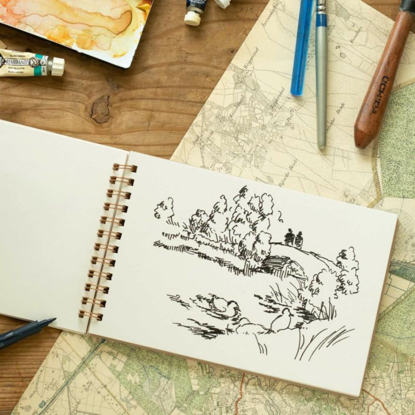 Open view of Penco sketch book B6 on drawing table with art supplies