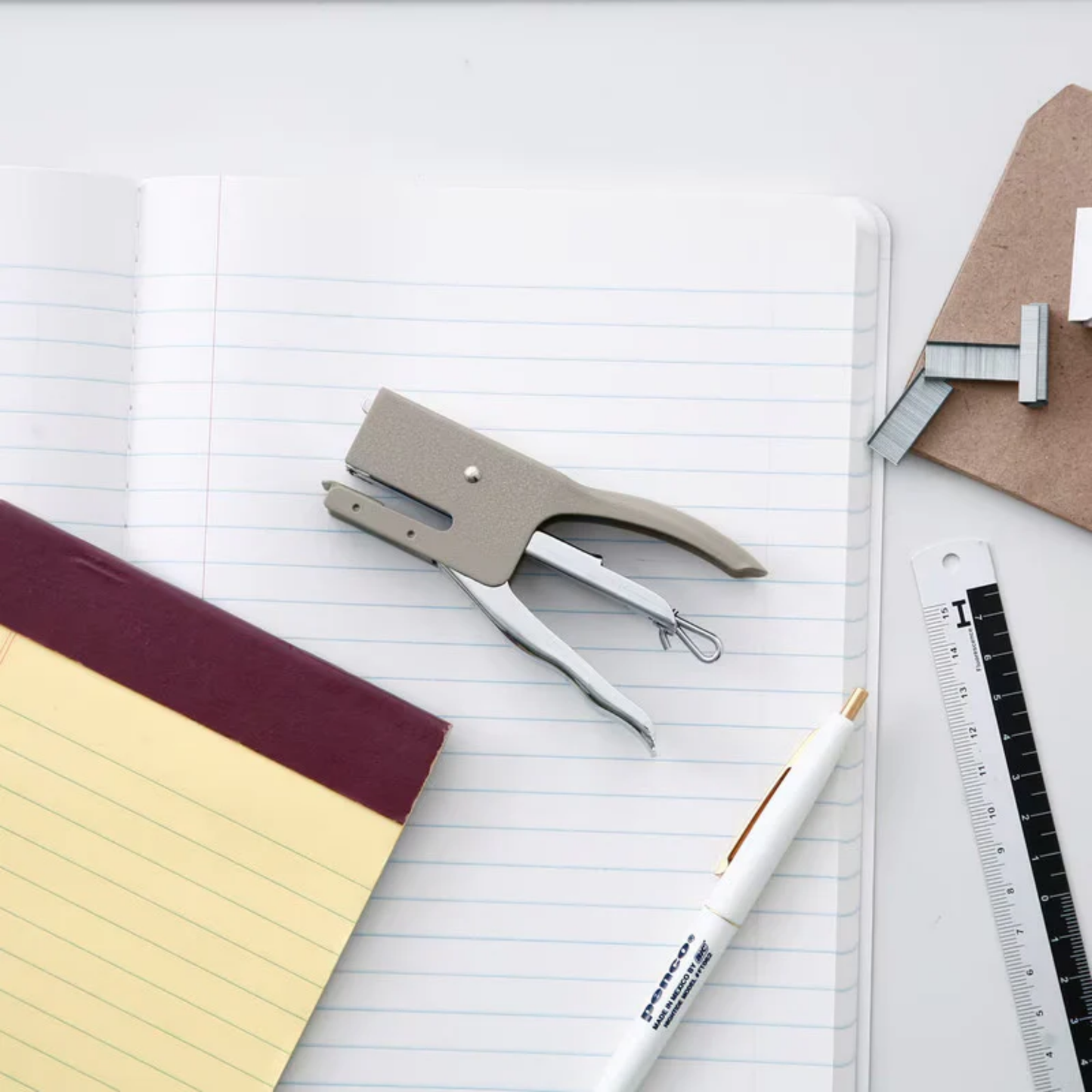 Penco stapler ivory on top of notebook surrounded by stationery