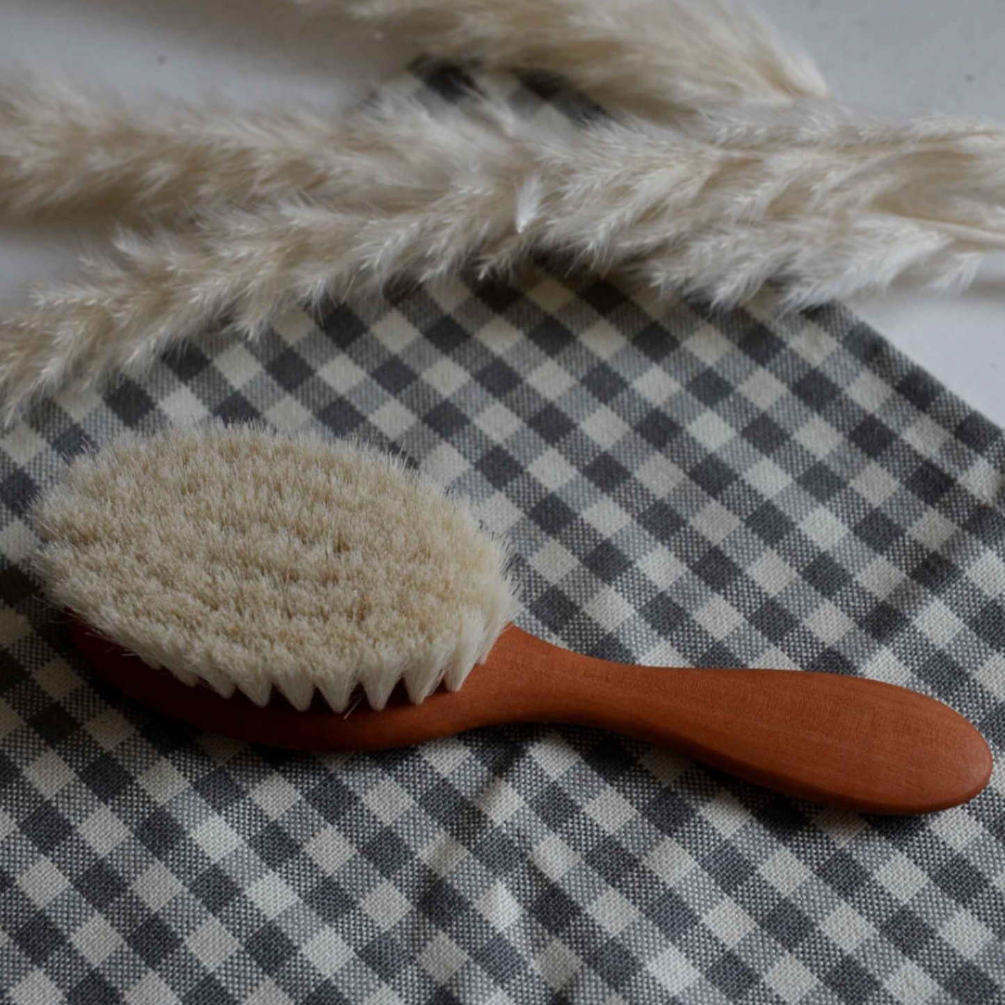 Redecker baby hair brush displayed on checkerd blanket with white flowers