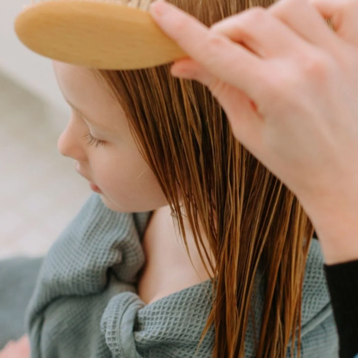 Woman using redecker child's hair brush on little girl wrapped in towel after shower