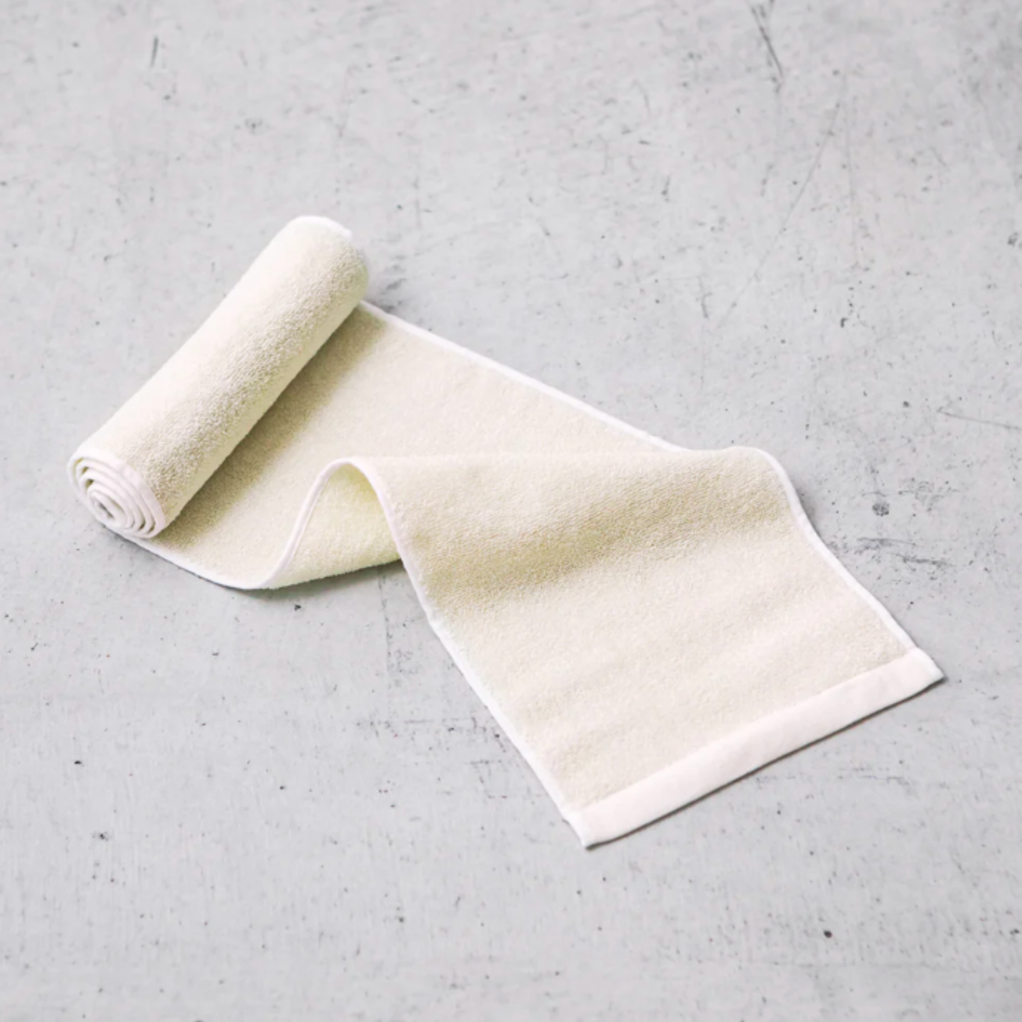 Sasawashi body scrub towel half unrolled on concrete tiled surface