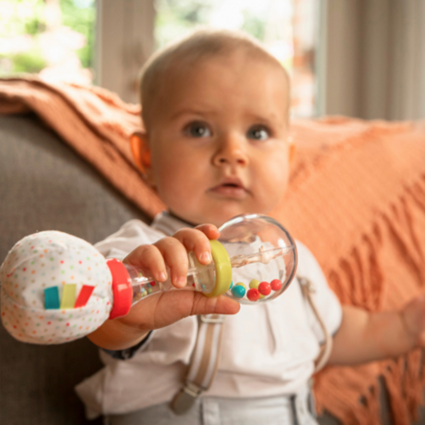 Baby playing with maracus rattle on couch with rattle in hand