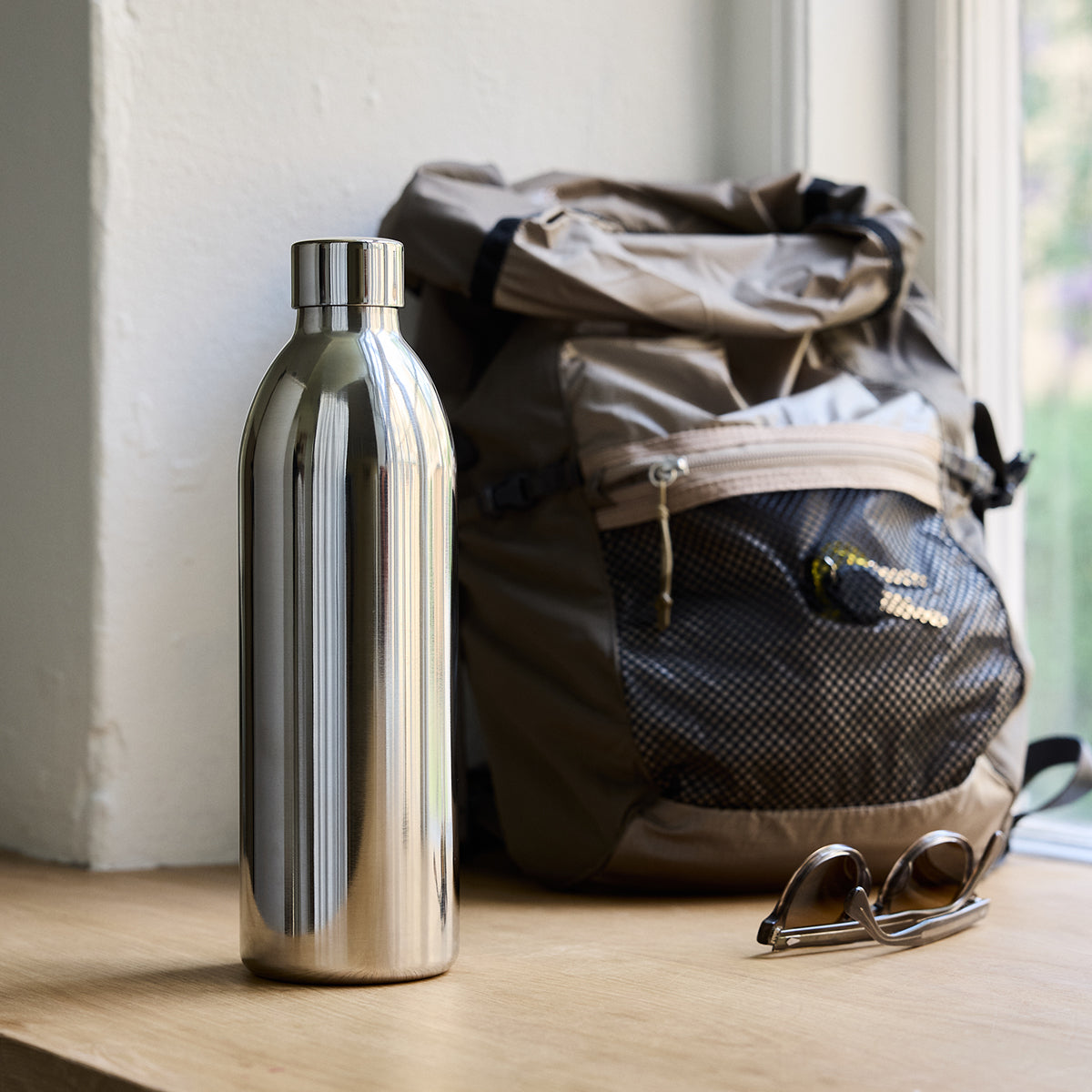 1000ml Stainless steel Carbonator 3 bottle on wood shelf in front of black bag and sunglasses