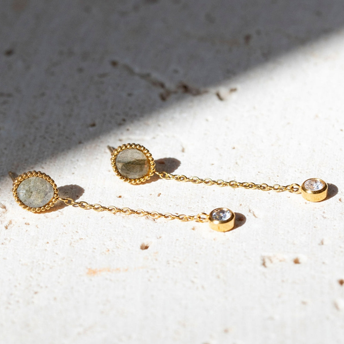 Close up of AEC Paris Clio Labradorite drop earrings laying on white textured stone