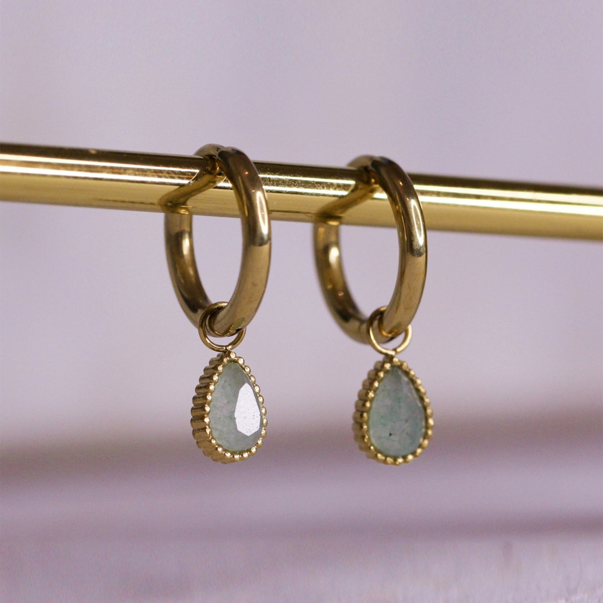Close up of AEC Paris Helios aventurine earrings hanging on brass rod 