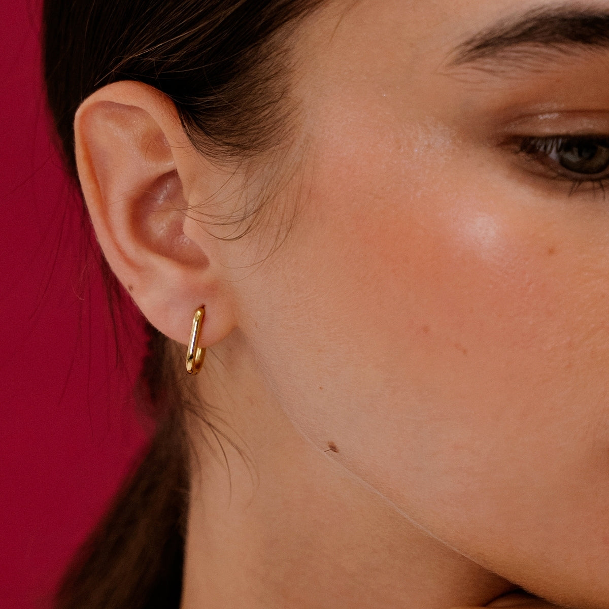Close up of woman wearing AEC Paris Zoya Gold earrings on red background