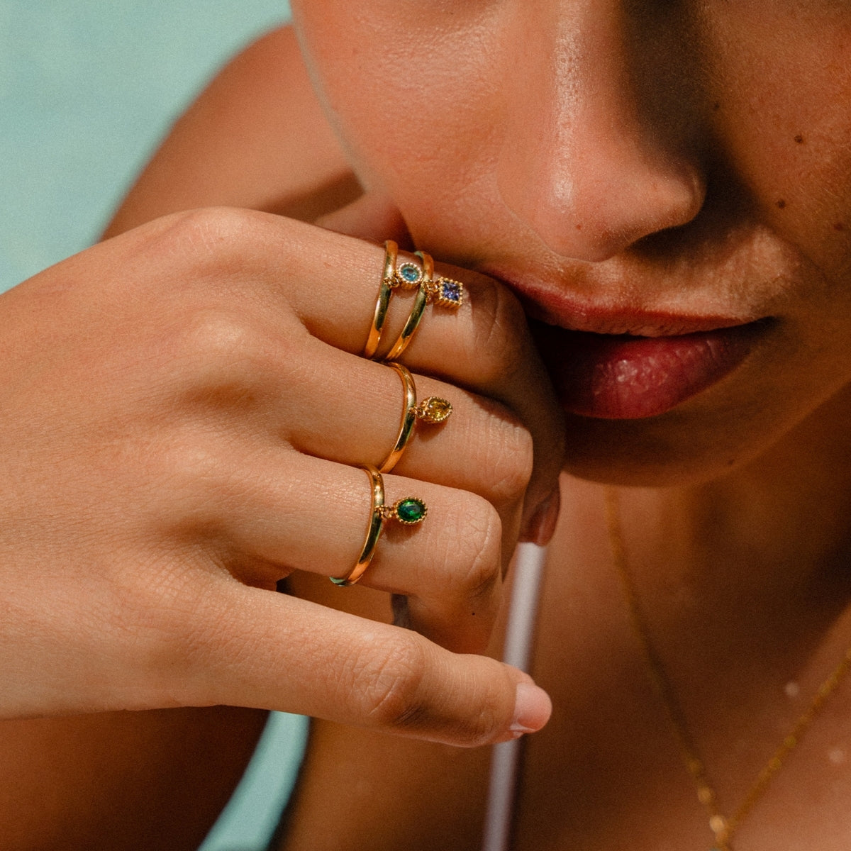 Woman with hand to her chin showing off AEC Paris Divya green zirconium oxide size 5-7 ring and 3 other rings