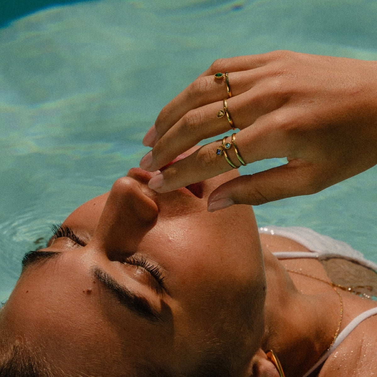 Woman laying in swimming with hand to her face wearing AEC Paris Divya yellow zirconium oxide size 5-7 ring and three other rings