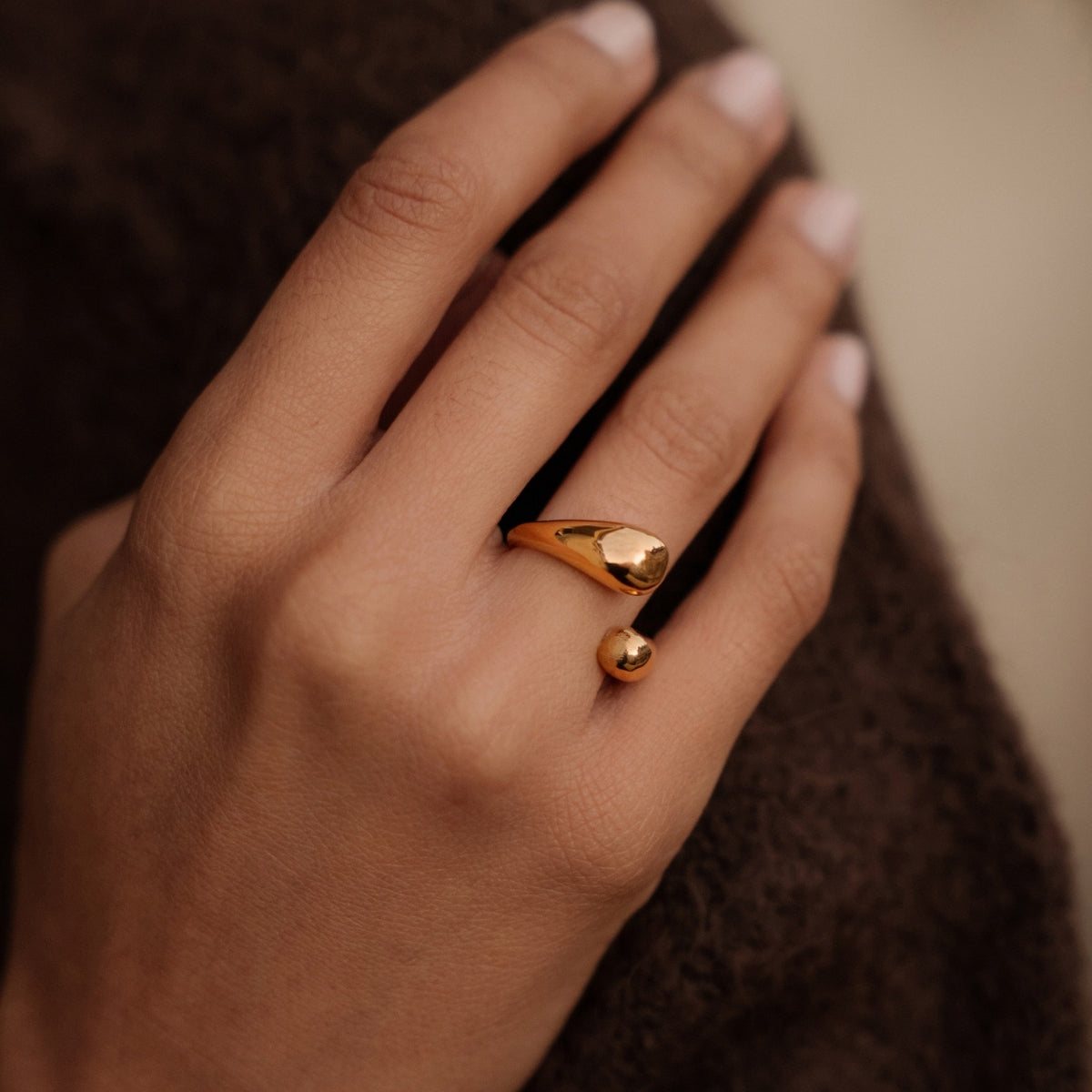 Close up of woman's hand wearing AEC Paris Irene Gold size 5-7 ring laying on brown jumper