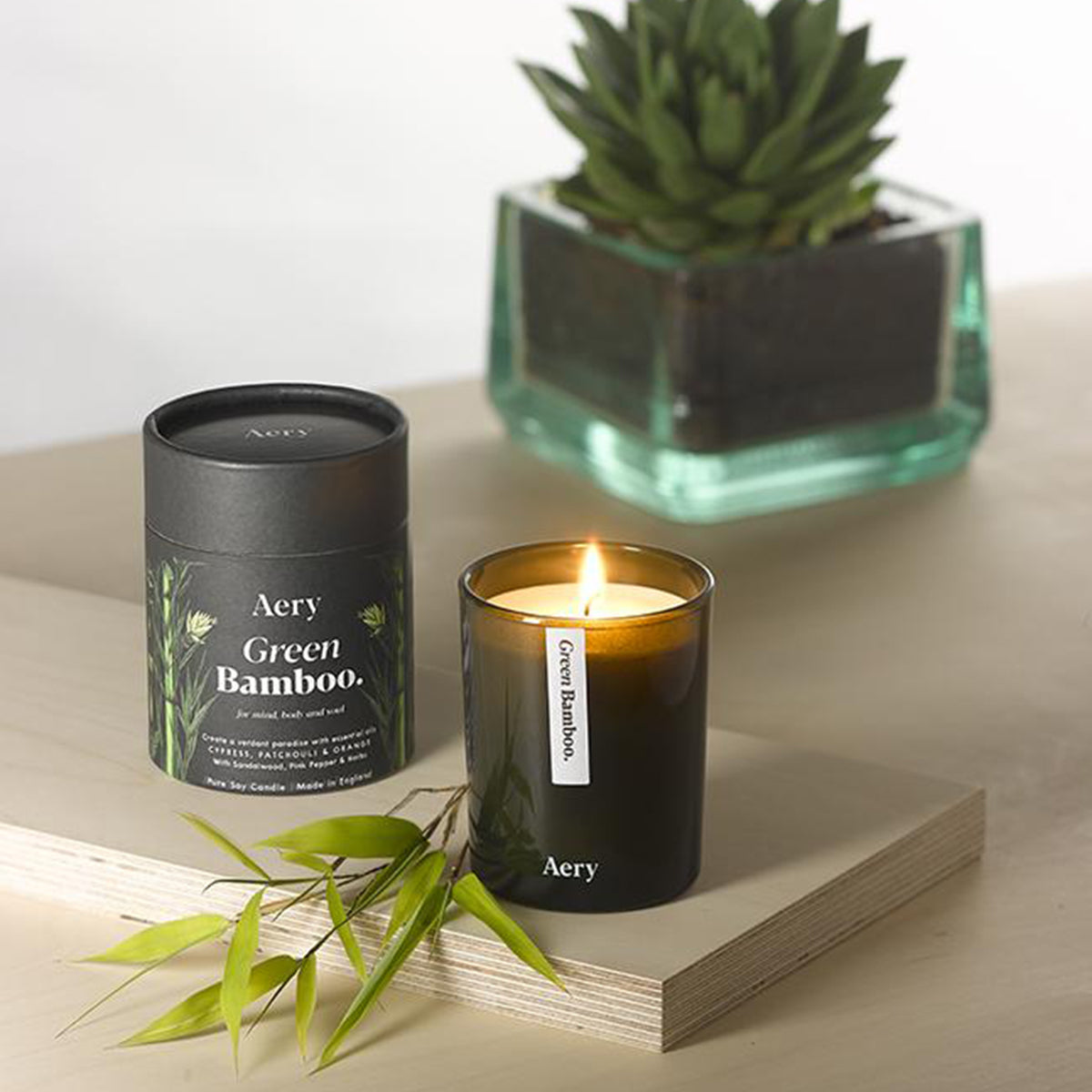 Aery Green Bamboo 200gm candle from the Botanical collection showing candle on a wooden sideboard with plants