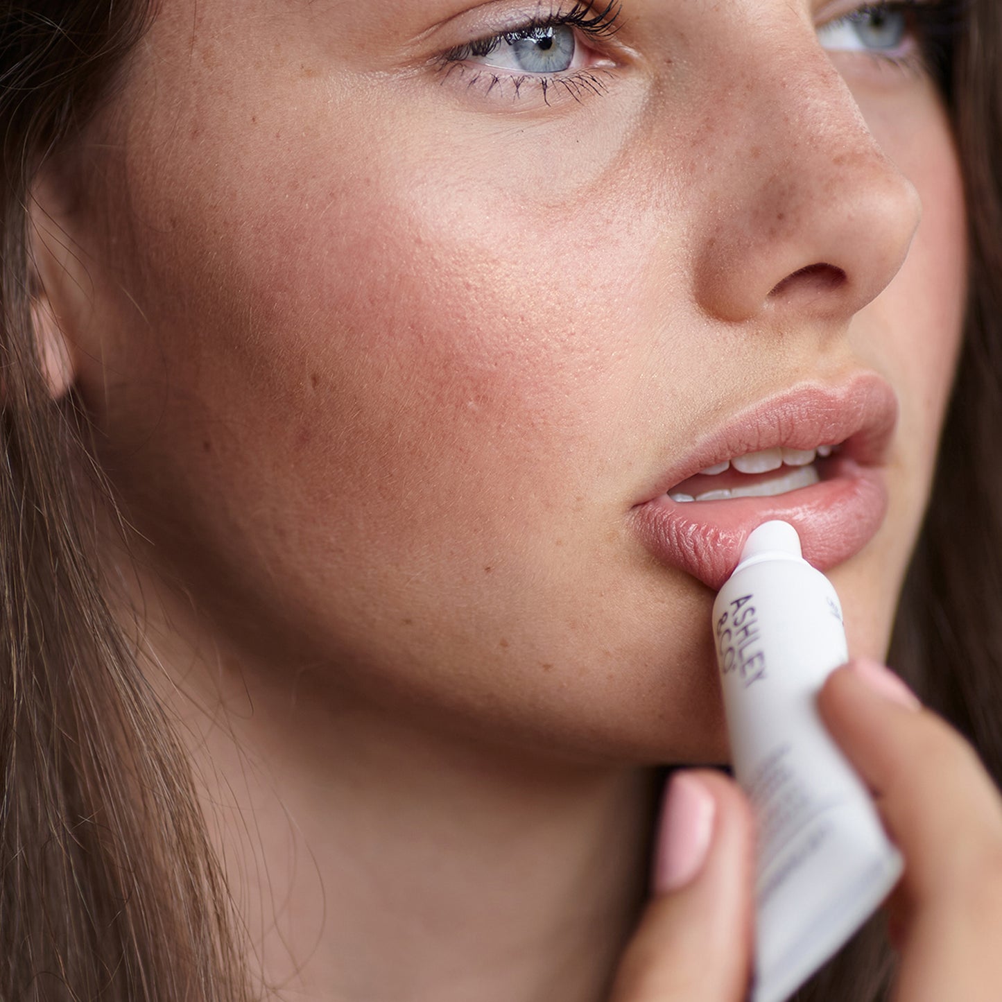 A young woman applying Ashley and Co 'Lip Punch' intensive lip balm.