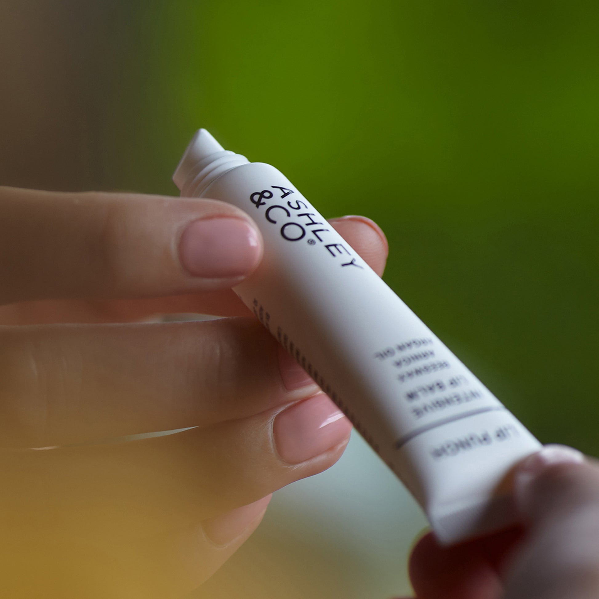 A person holding a tube of Ashley and Co 'Lip Punch' intensive lip balm.