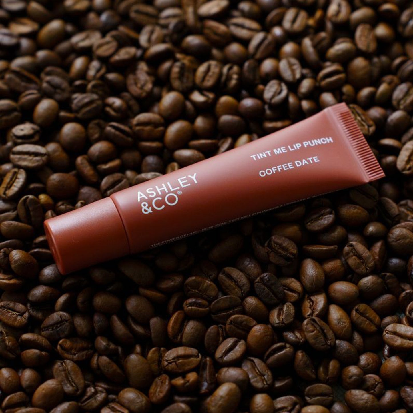 Ashley and Co 'Tint Me Lip Punch' coffee date coloured lip balm laying on coffee beans.