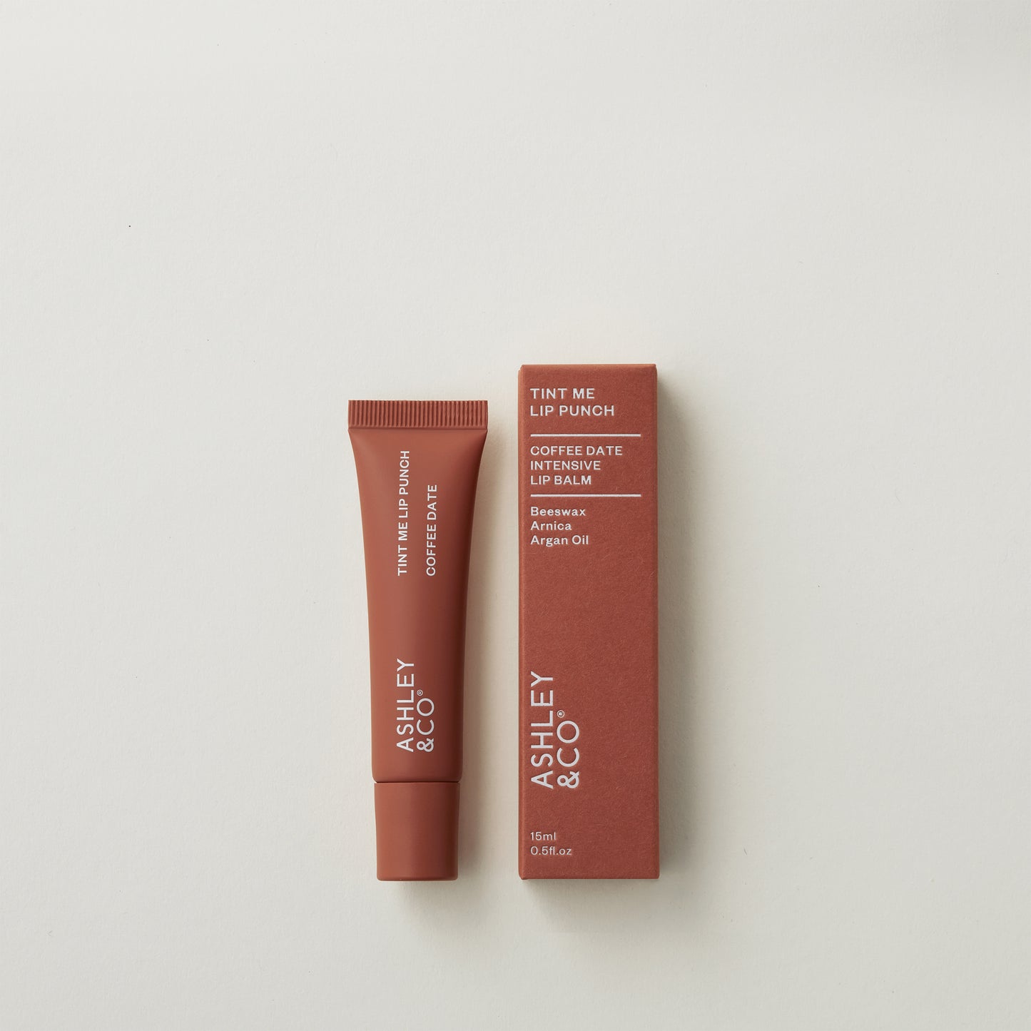 Ashley and Co 'Tint Me Lip Punch' coffee date coloured lip balm on a grey background.