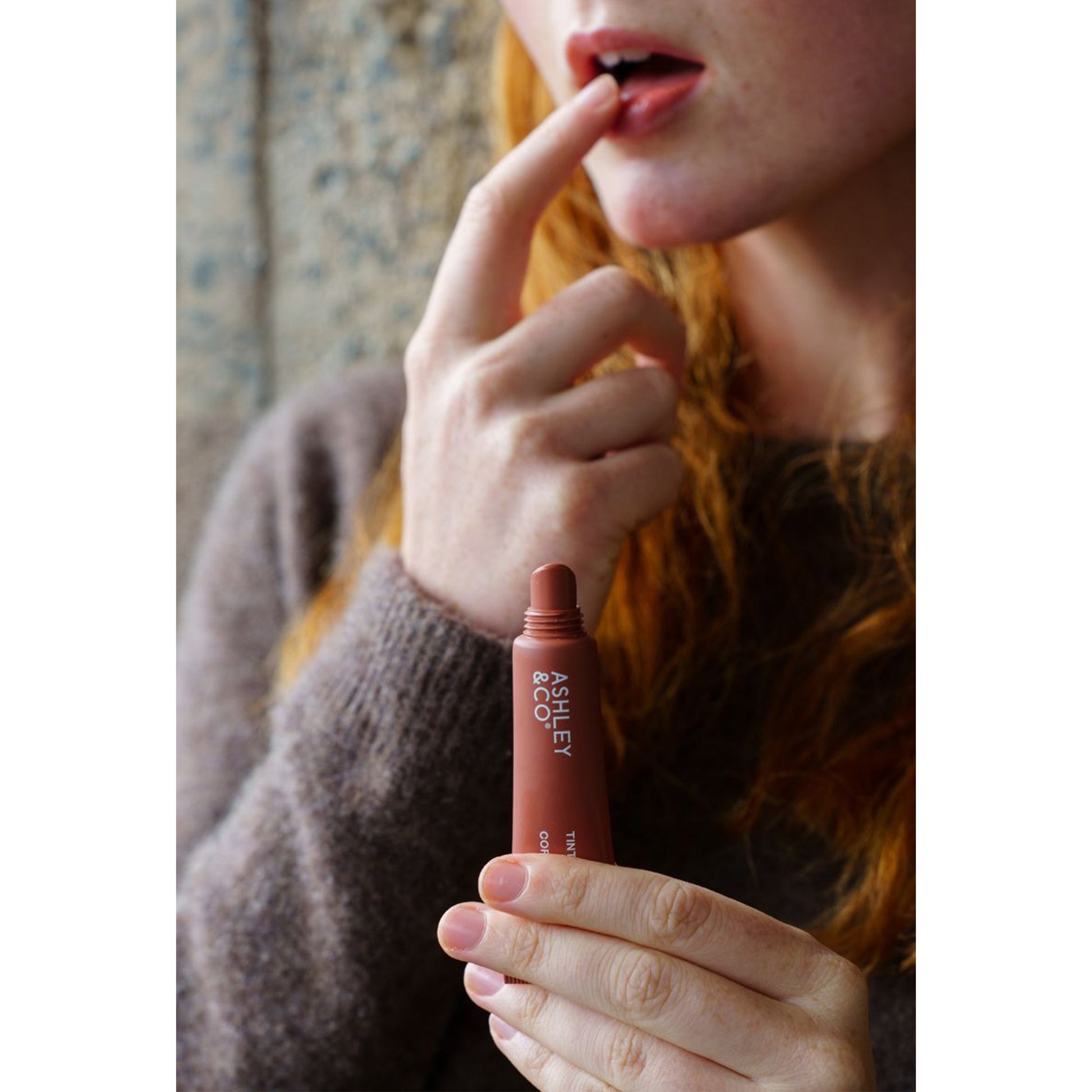 Ashley and Co 'Tint Me Lip Punch' coffee date coloured lip balm being applied to a woman's lips.