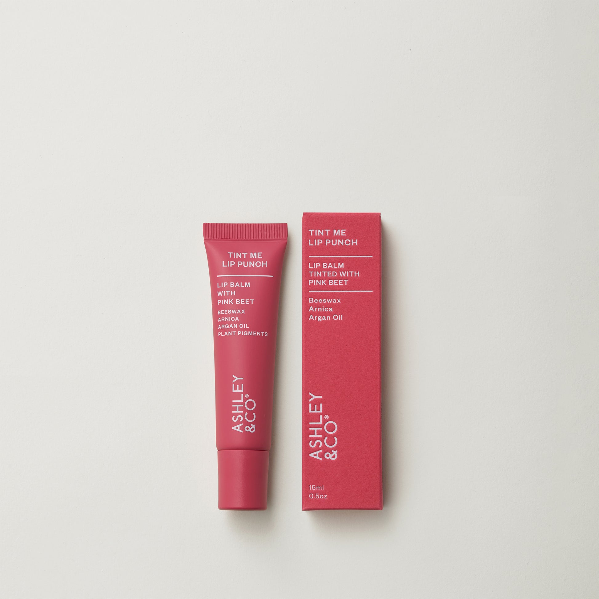 Ashley and Co 'Tint Me Lip Punch' pink coloured lip balm on a grey background.