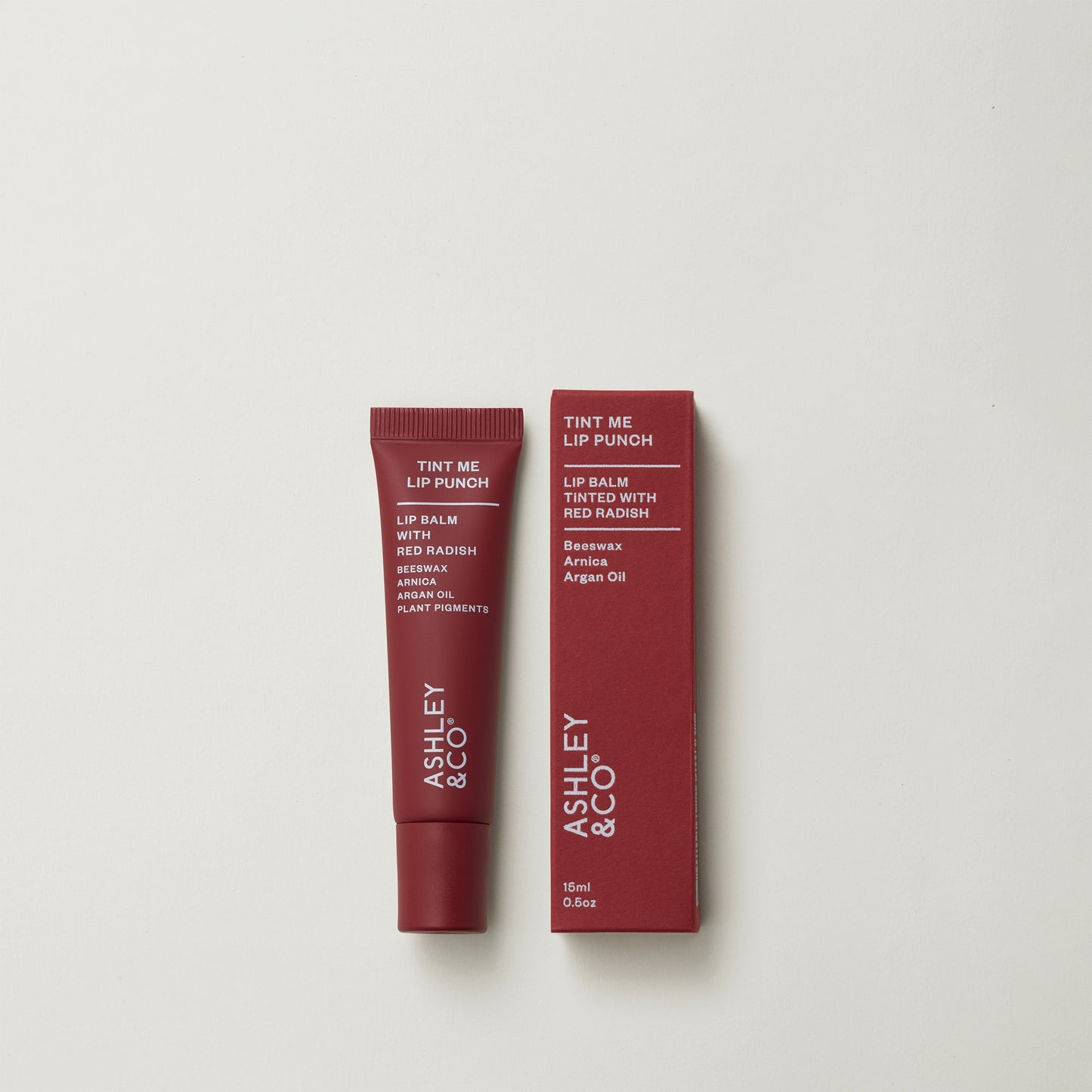 Ashley and Co 'Tint Me Lip Punch' beet red coloured lip balm on a grey background.