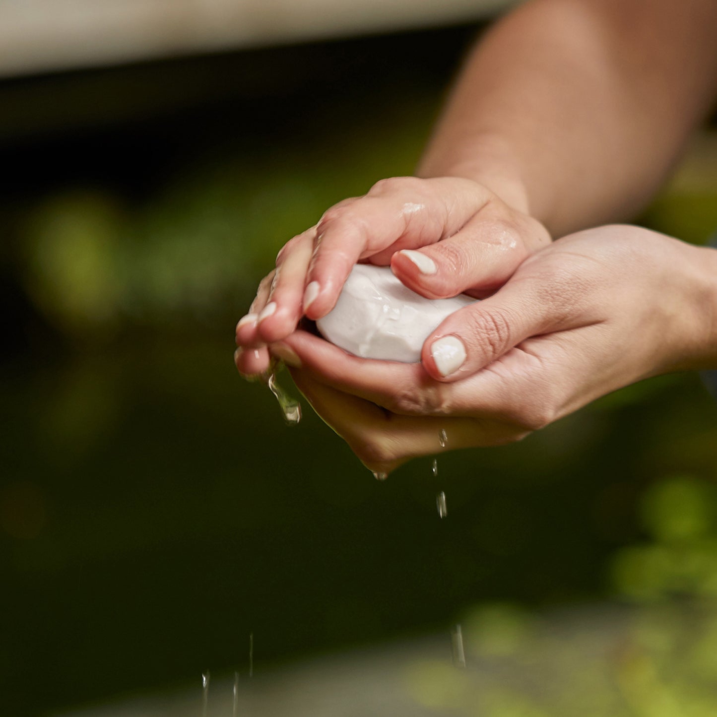 A person washing their hands using Ashley and Co 'Mini Bar' body soap in parakeets and pearls fragrance.