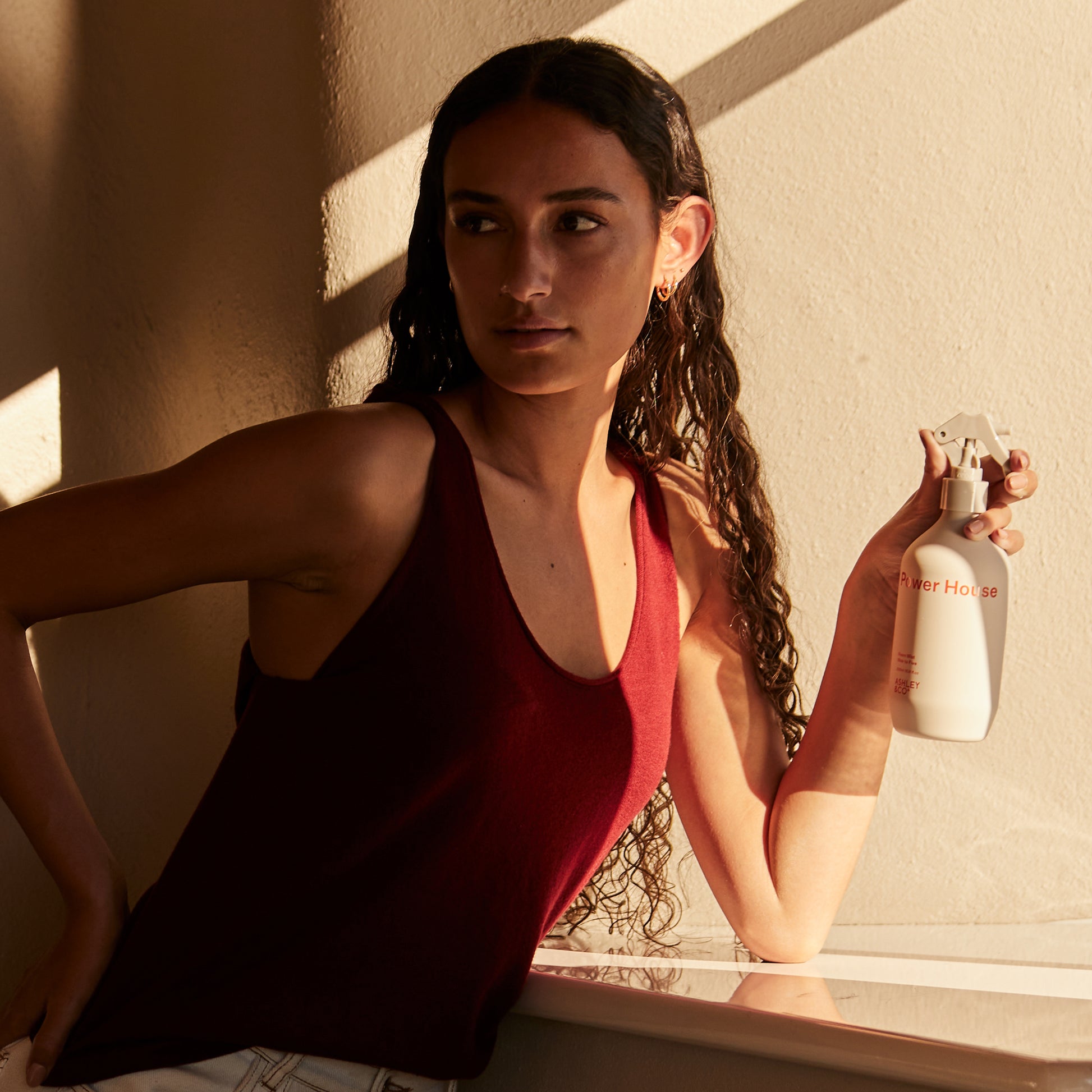 A woman holding a bottle of Ashley and Co 'Power House' room mist in nine to five fragrance.