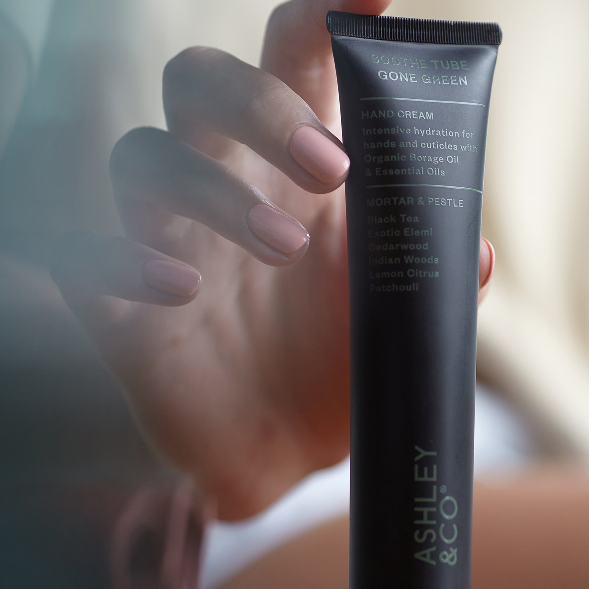 Close up shot of a woman holding Ashley and Co 'Soothe Tube Gone Green' handcream in mortar and pestle fragrance.